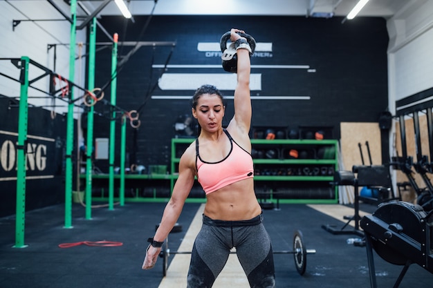 Mujer joven, entrenamiento, balanceo, kettlebell, interior, en, un, crossfit, gimnasio