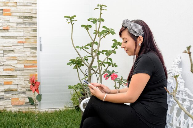 Mujer joven enviando mensajes de texto sentada en el patio de su casa