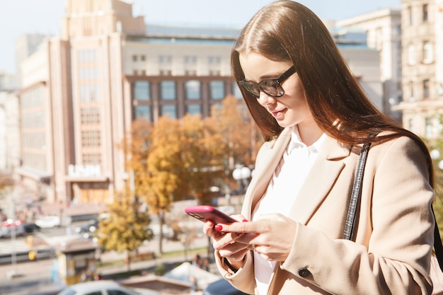 Mujer joven enviando mensajes de texto en su teléfono smar, disfrutando de un cálido día de otoño, espacio de copia