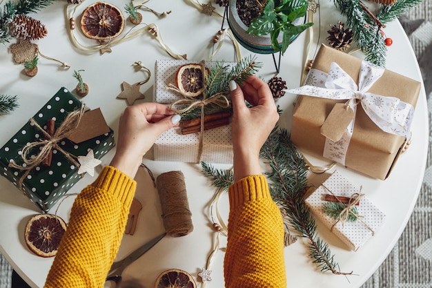 Mujer joven envolver y decora el regalo de Navidad en la mesa