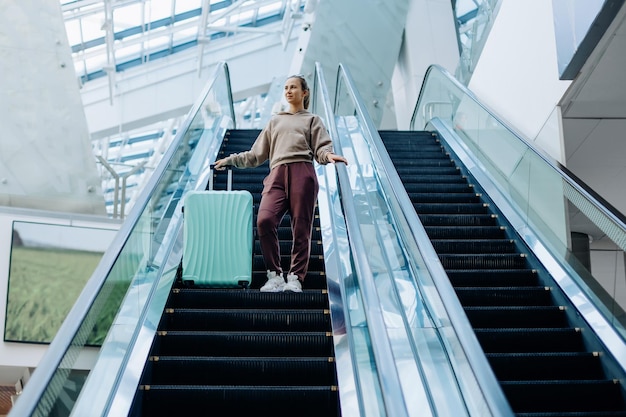 mujer joven, con, equipaje, posición, en, el, escalera mecánica, en, el, aeropuerto