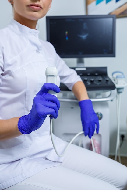 Una mujer joven es una médica interna que lleva un traje blanco y guantes médicos sosteniendo una sonda de ultrasonido en sus manos diagnóstico de ultrasonido enfoque selectivo