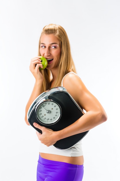 Mujer joven con escala debajo de su brazo y manzana