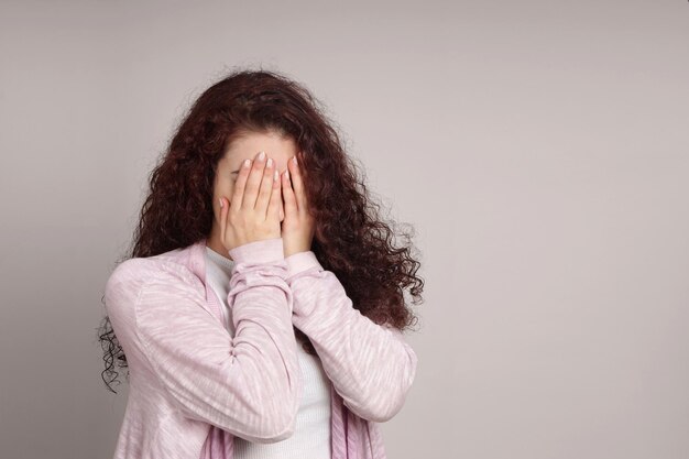 Foto mujer joven escondiendo la cara mientras está de pie contra la pared