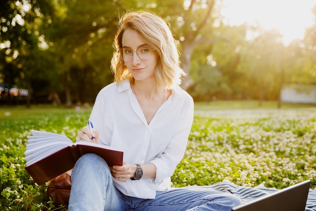 Mujer joven escribiendo algo en el cuaderno en el parque