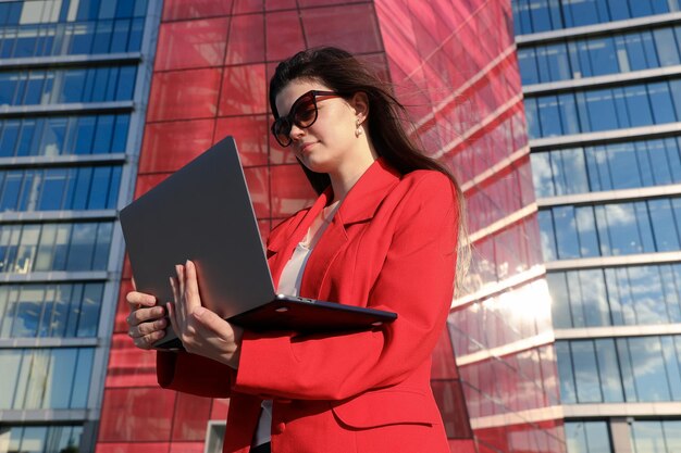 Mujer joven escribiendo en una computadora portátil frente a un edificio de oficinas