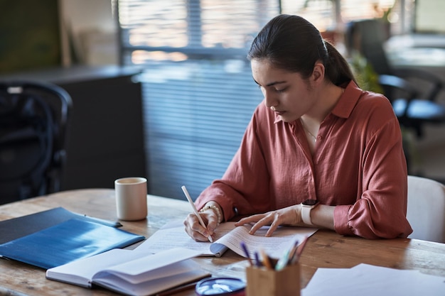 Mujer joven escribiendo en un cuaderno mientras trabaja en el escritorio