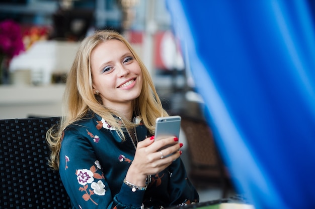 Mujer joven escribiendo un mensaje en un teléfono celular en un café de la calle