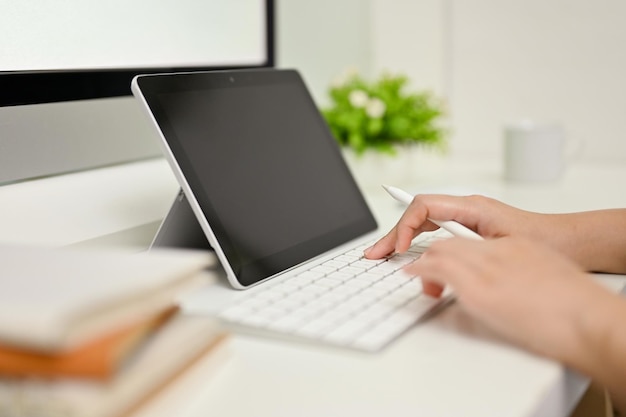 Mujer joven escribiendo en el teclado mientras trabaja con una tableta en la oficina