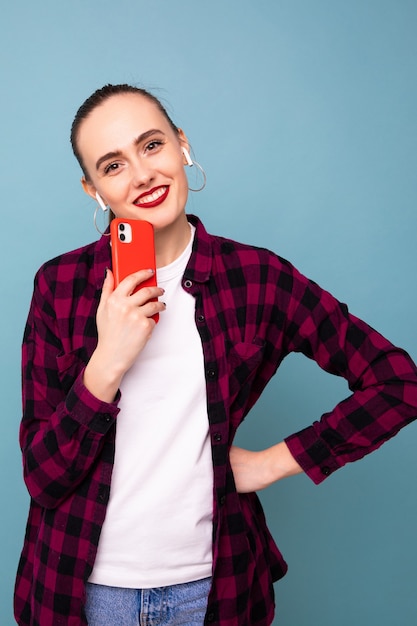 Una mujer joven escucha música desde su teléfono sobre un fondo azul.