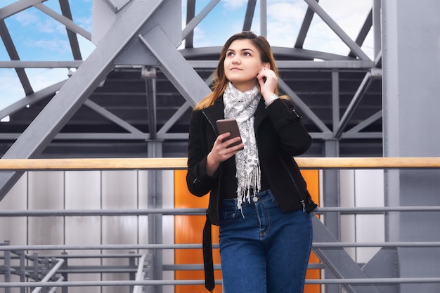 Mujer joven escucha música y sueña entre las estructuras urbanas del paso elevado cubierto