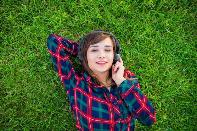 Una mujer joven escucha música con sus auriculares sobre un césped