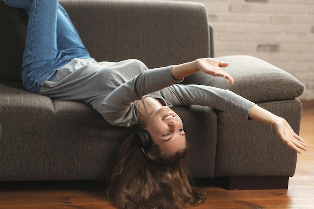 Mujer joven escuchando música con auriculares acostado en un sofá en la habitación