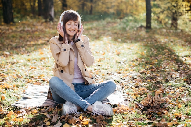 Mujer joven escuchando música con auriculares en el bosque de otoño