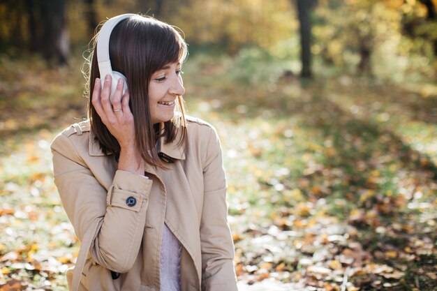 Mujer joven escuchando música con auriculares en el bosque de otoño