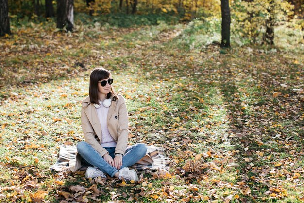 Mujer joven escuchando música con auriculares en el bosque de otoño