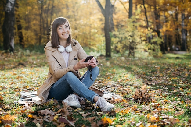 Mujer joven escuchando música con auriculares en el bosque de otoño