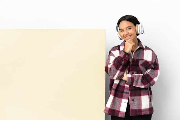 Mujer joven escuchando música con un gran cartel vacío sobre fondo aislado feliz y sonriente