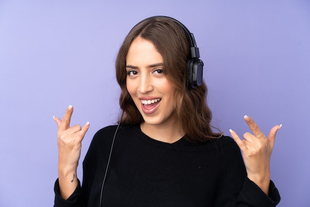 Mujer joven escuchando música haciendo gesto de rock