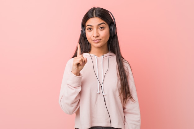 Mujer joven escuchando música mostrando el número uno con el dedo