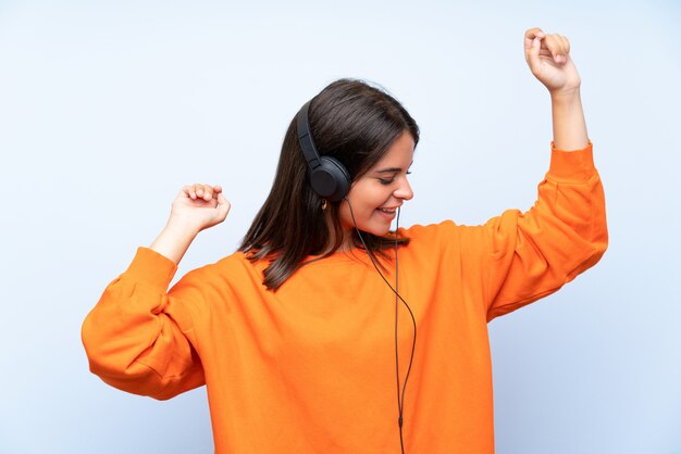 Mujer joven escuchando música con un móvil y bailando sobre la pared azul aislada