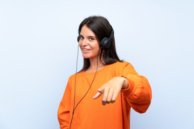 Foto mujer joven escuchando música con un móvil sobre una pared azul aislada te señala con una expresión segura