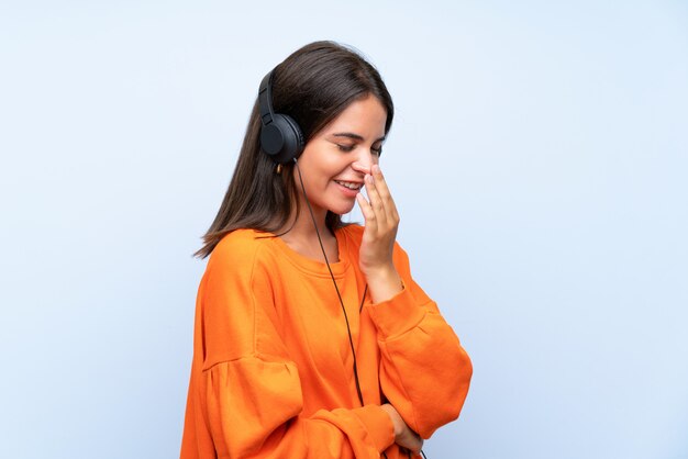 Mujer joven escuchando música con un móvil sobre pared azul aislado sonriendo mucho