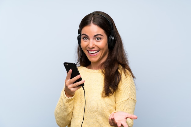 Mujer joven escuchando música con un móvil sobre pared azul aislado