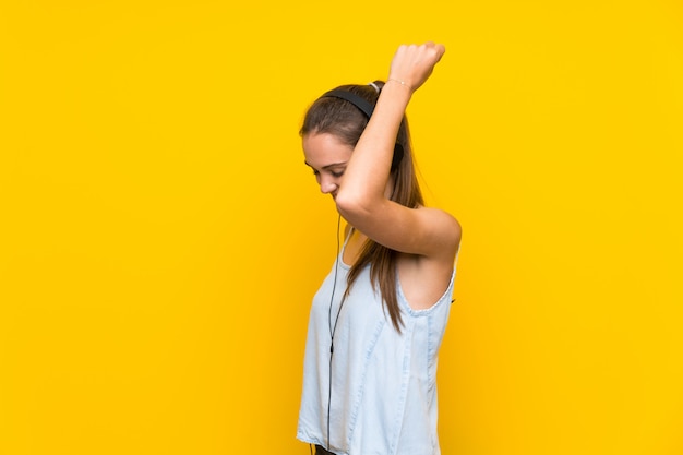 Mujer joven escuchando música en la pared amarilla