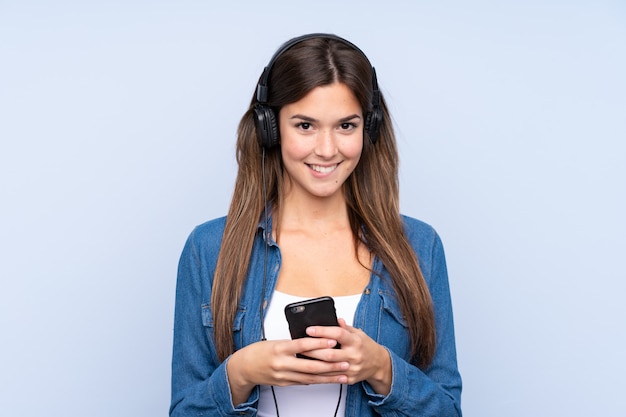 Mujer joven escuchando música sobre pared aislada