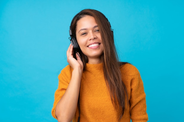 Mujer joven escuchando música sobre pared azul