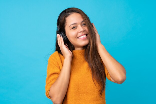 Mujer joven escuchando música sobre pared azul