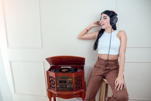 Mujer joven escuchando música con tocadiscos vintage en la sala de estar