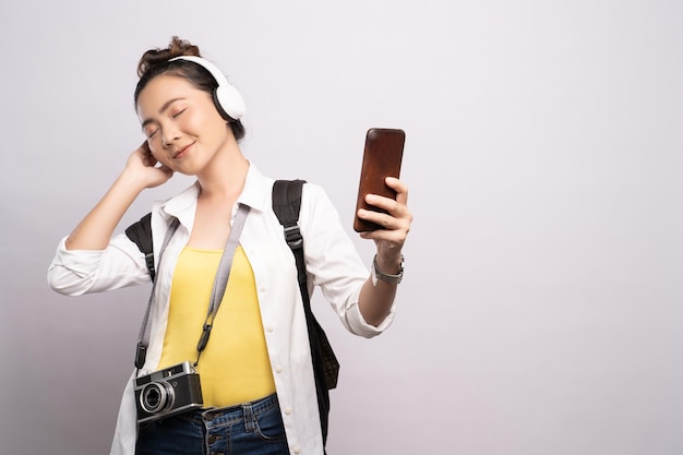 Mujer joven escuchando música a través de auriculares mientras está de pie contra un fondo blanco