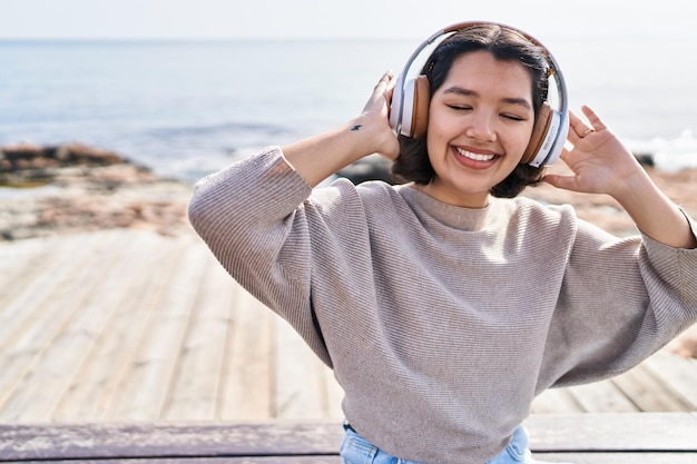 mujer joven, escuchar música, sentado, en, banco, en, playa