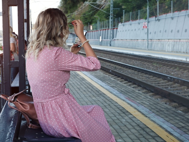 Mujer joven esperando en la plataforma del tren arreglando su maquillaje