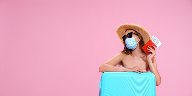 Mujer joven esperando el vuelo sentada en el suelo cerca de su maleta con mascarilla para prevenir coron ...