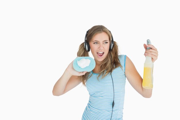 Mujer joven con esponja y botella de spray disfrutando de la música con auriculares