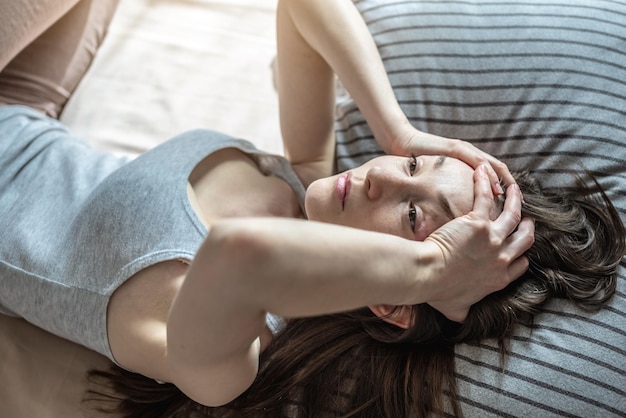 La mujer joven está acostada en la cama y sosteniendo su cabeza con las manos experimentando un dolor de cabeza migraña Concepto de insomnio causado por el estrés, la ansiedad y los problemas