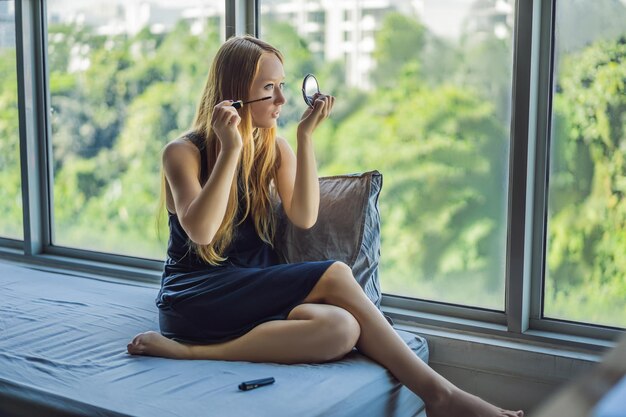 Mujer joven está aplicando maquillaje frente a la ventana en el apartamento de estudio de belleza Maquillaje profesional peinado Tono de piel Maquillaje de color brillante con pestañas largas y piel fresca y joven