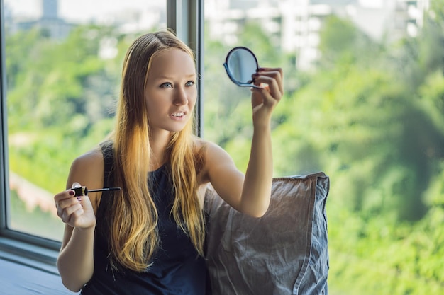 Mujer joven está aplicando maquillaje frente a la ventana en el apartamento de estudio de belleza Maquillaje profesional peinado Tono de piel Maquillaje de color brillante con pestañas largas y piel fresca y joven