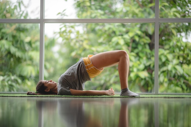 Una mujer joven está aprendiendo yoga en casa mediante el uso de videos de entrenamiento en línea, una chica sexy y linda se relaja con el deporte y el ejercicio remoto, el estilo de vida, el hogar interior, el concepto de cuarentena aislada en el hogar.