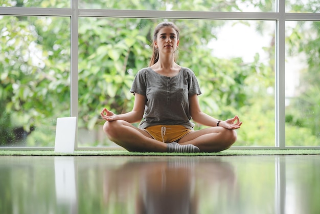 Una mujer joven está aprendiendo yoga en casa mediante el uso de videos de entrenamiento en línea, una chica sexy y linda se relaja con el deporte y el ejercicio remoto, el estilo de vida, el hogar interior, el concepto de cuarentena aislada en el hogar.