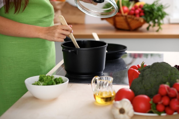 Mujer joven está cocinando junto a la estufa en la cocina de cerca