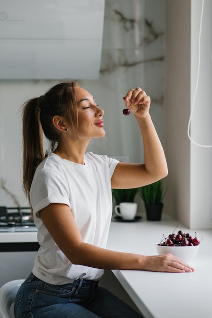 Mujer joven está comiendo una cereza dulce Retrato de una chica hermosa con una cereza en la cocina