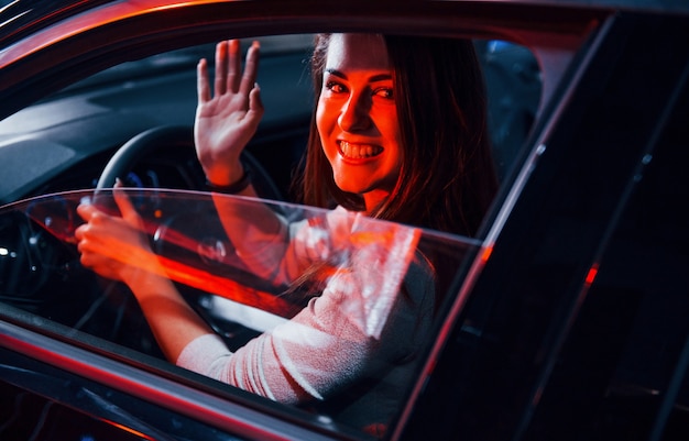 La mujer joven está dentro de un automóvil moderno nuevo con iluminación roja.