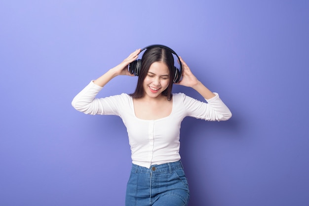 La mujer joven está escuchando música en fondo púrpura