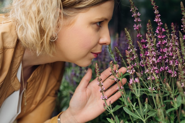 Mujer joven está feliz de oler flores fragantes en la ventana de la calle de la tienda de flores. Obra de floristería. Aromaterapia. Hierbas y plantas medicinales.