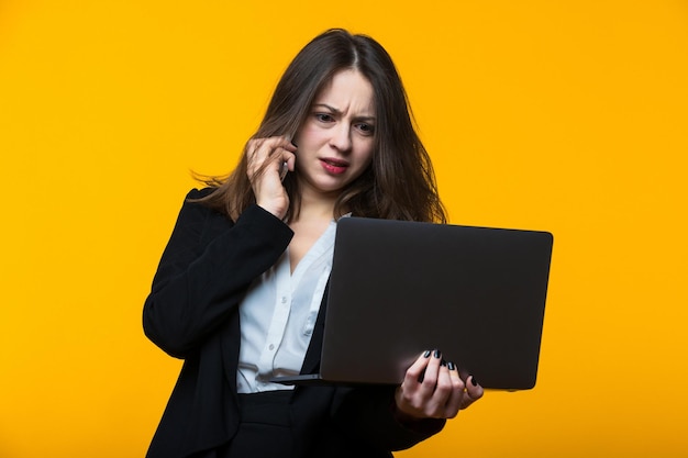 Una mujer joven está hablando por teléfono y mirando la pantalla del portátil.