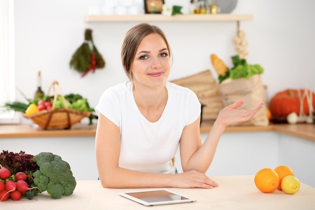 Mujer joven está haciendo compras en línea por computadora de tableta y tarjeta de crédito Ama de casa encontró una nueva receta para cocinar en una cocina